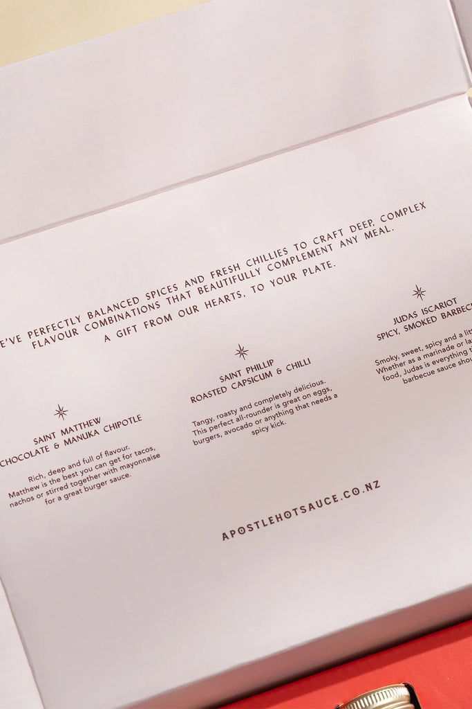 Close-up of Apostle Hot Sauce gift box interior showing flavour descriptions for Saint Matthew (Chocolate & Manuka Chipotle), Saint Phillip (Roasted Capsicum & Chilli), and Judas Iscariot (Spicy Smoked Barbecue).