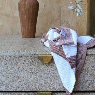 A soft, textured tea towel in brown and white stripes draped over a stone drawer unit, with a tall, earthy-toned vase in the background.