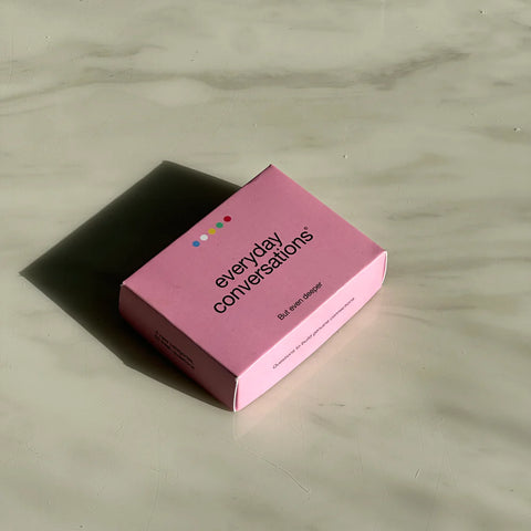 Pink box of “Everyday Conversations” card game resting on a marble surface, designed to spark deeper daily dialogue