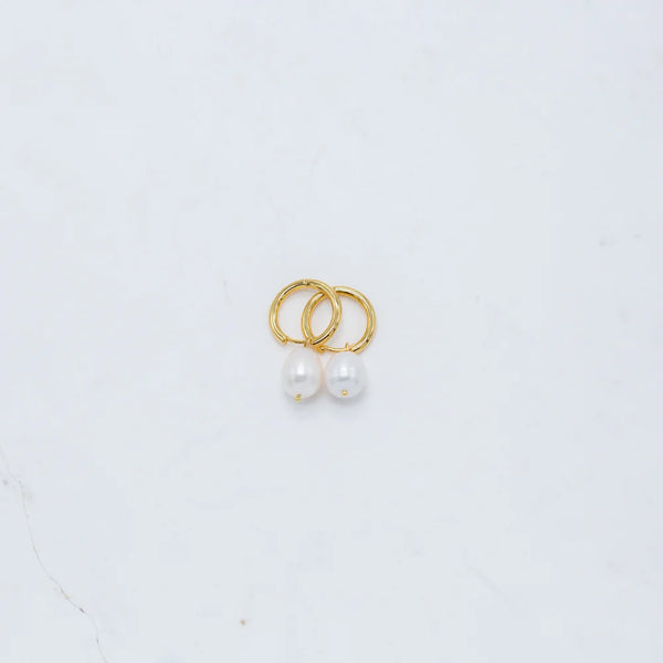 Gold hoop earrings with freshwater pearl drops, photographed on a white marble background.
