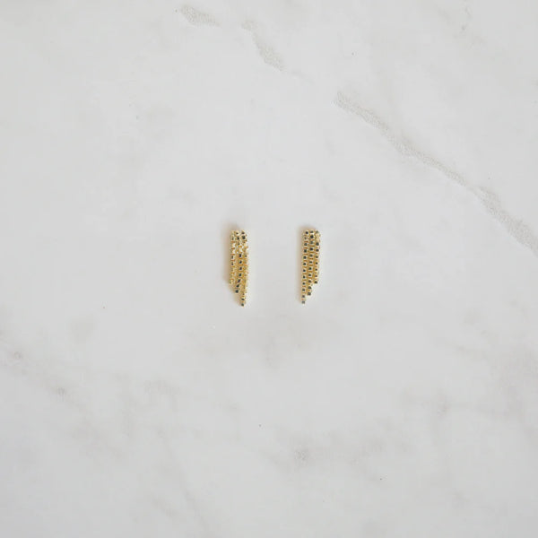 Gold crystal mesh fringe stud earrings laid flat on a white marble surface, showcasing their elegant drape and sparkle.