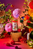 Jar of Apostle Lavender & Rosemary Hot Honey styled with vibrant florals and habanero chillies, set against a rich pink and orange backdrop