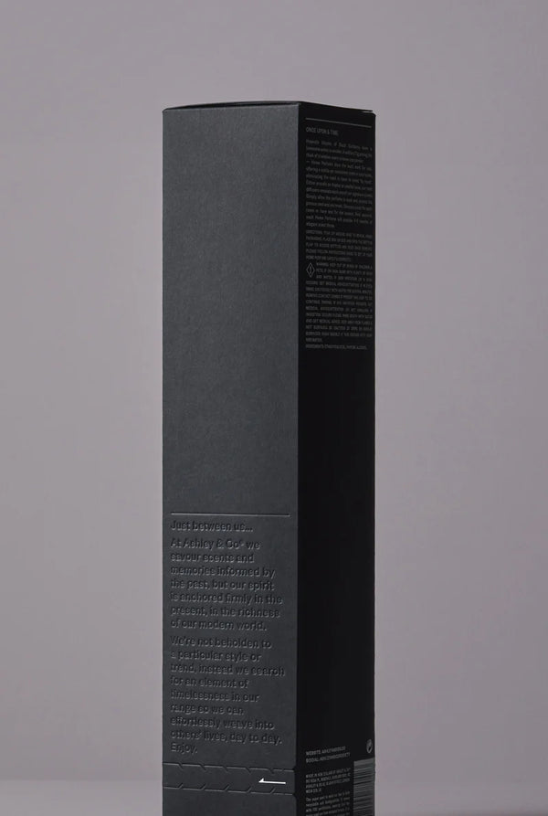 Side view of Ashley & Co diffuser packaging in matte black with embossed brand story and product details on a neutral backdrop.