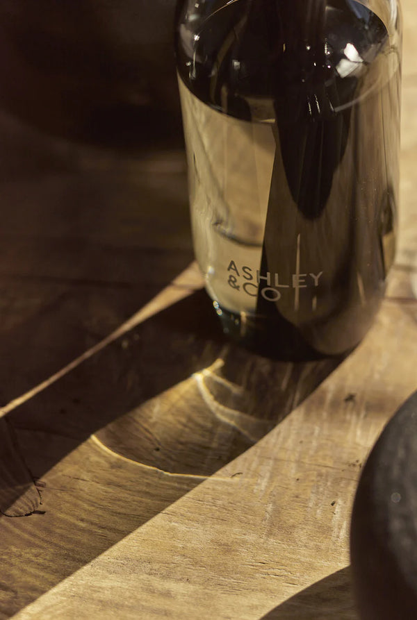 Ashley & Co black glass diffuser casting warm shadows on a wooden surface, luxury home fragrance with moody, natural lighting.