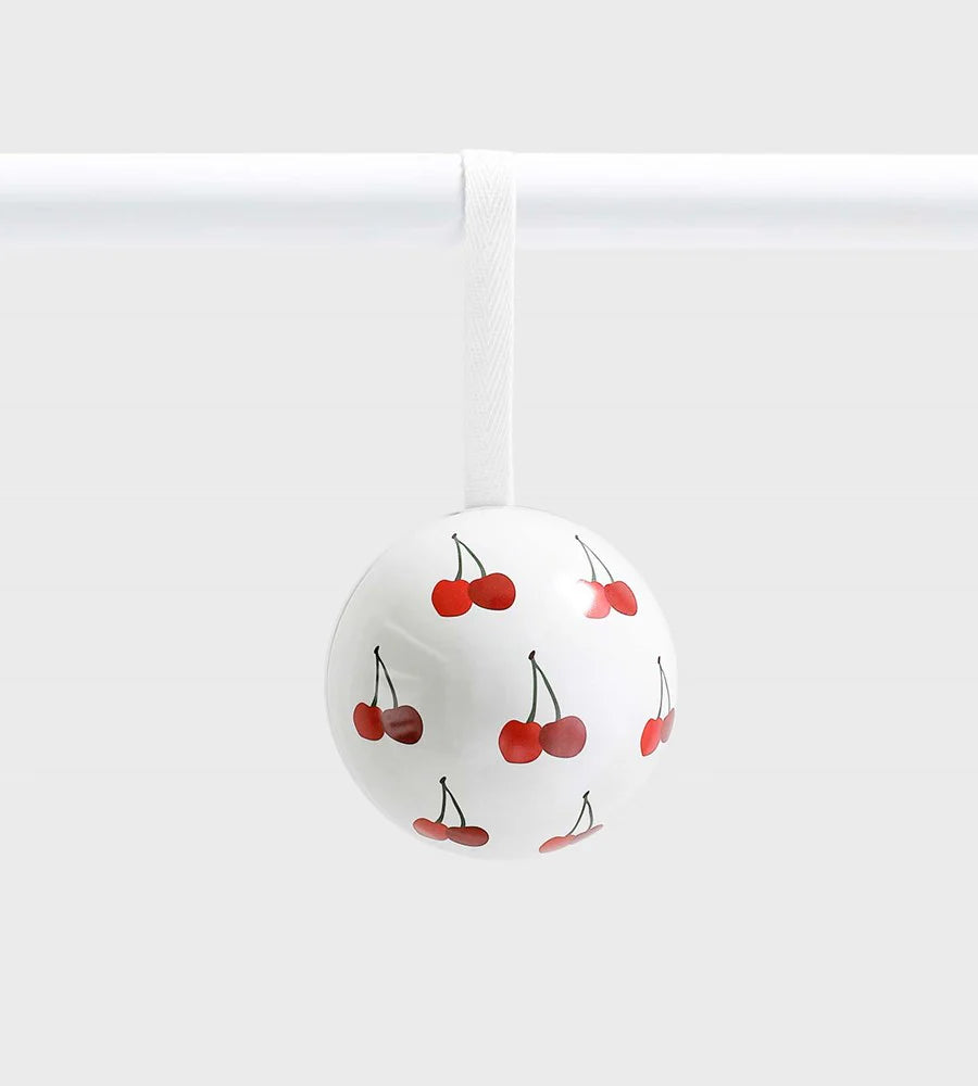White ceramic ornament decorated with a repeating red cherry pattern, hanging from a white ribbon against a light grey background