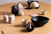Contemporary black ceramic bowl displayed on a wooden dining table with matching minimalist tableware – modern dinnerware styling inspiration.