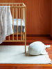 Grey striped whale soft toy placed beside a wooden cot in a warm-toned nursery, styled on a cream rug for a cosy, playful touch.