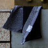 Close-up of single black and grey waffle towel hanging over stone ledge with visible woven texture.
