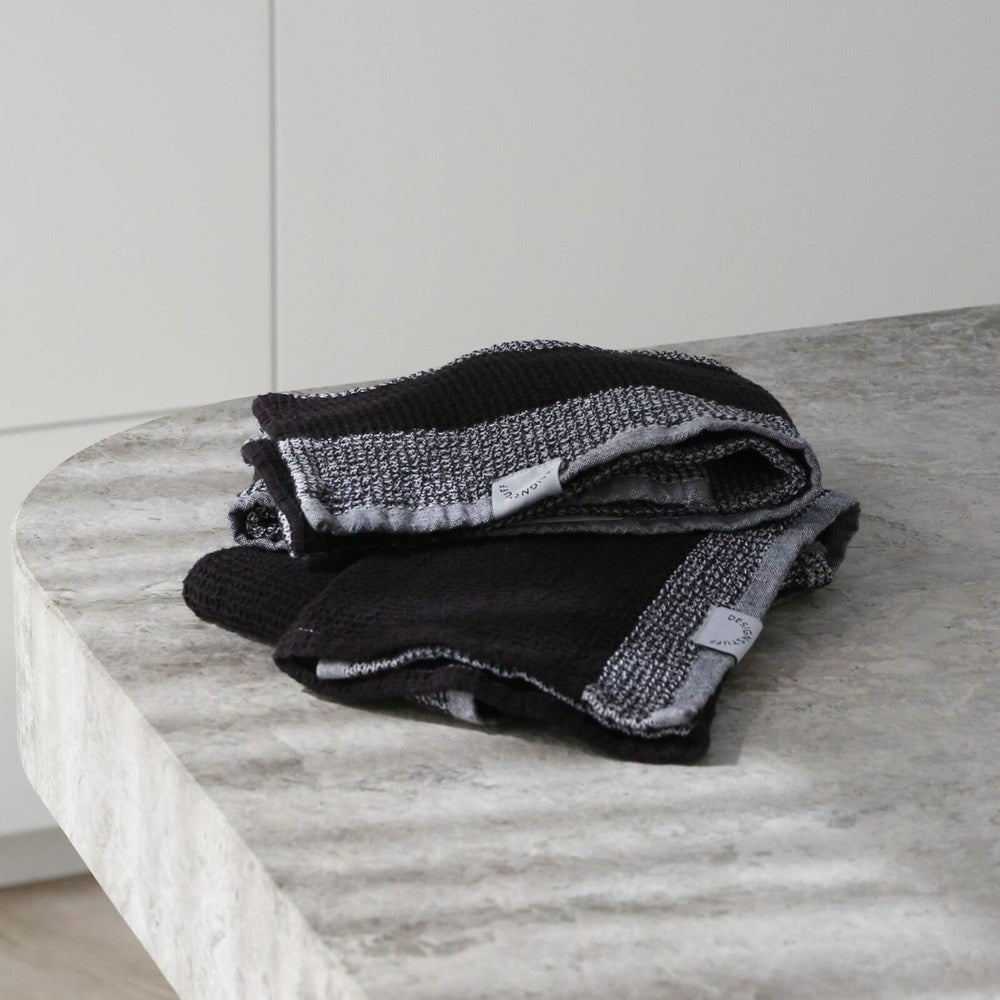 Pair of black and grey waffle tea towels with "Designstuff" label, folded on a marble bench.