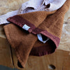 A close-up of two waffle weave tea towels in warm brown and burgundy hues, one showing a visible “Designstuff” tag, styled casually on a rustic wooden surface.