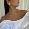 Woman wearing statement gold ripple earrings and a gold flat snake chain necklace, styled with an off-shoulder white top