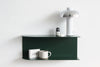 A dark green floating shelf mounted on a white wall, styled with a white mushroom-shaped table lamp, a white ceramic mug, a small box, and a candle.
Made in NZ