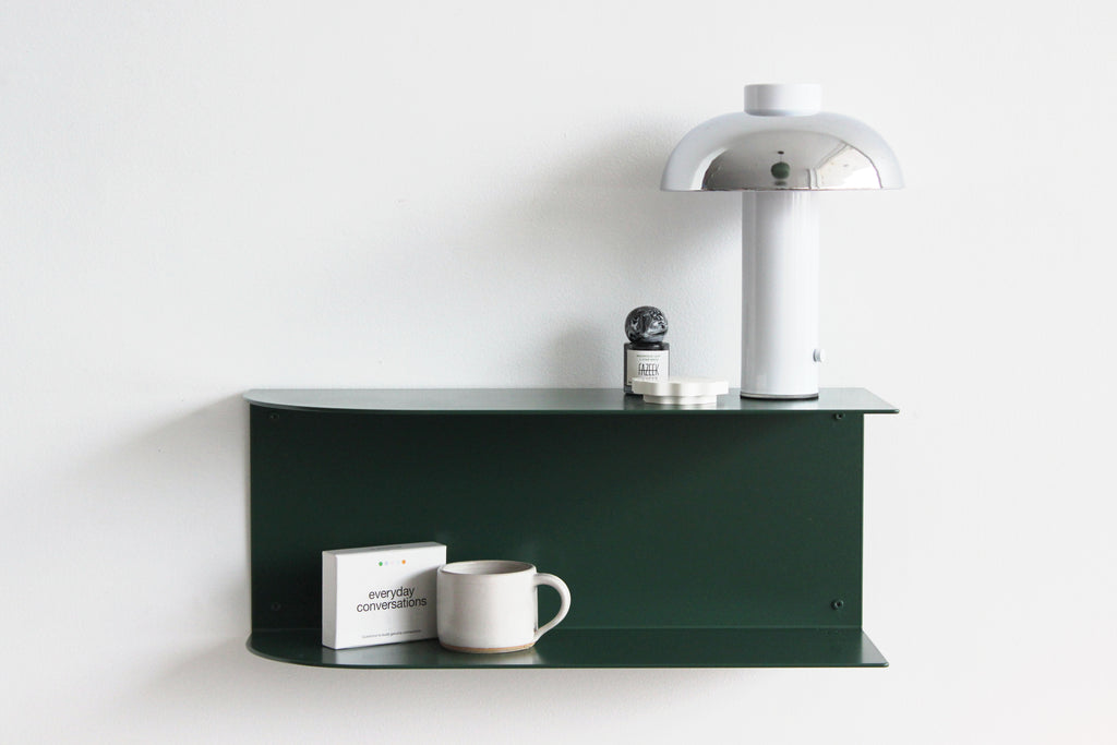 A dark green floating shelf mounted on a white wall, styled with a white mushroom-shaped table lamp, a white ceramic mug, a small box, and a candle.
Made in NZ