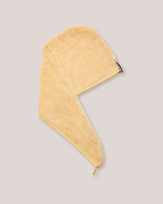 A light yellow cotton towel with a triangular flap and a small black brand tag, shown on a solid gray background.