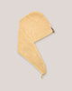 A light yellow cotton towel with a triangular flap and a small black brand tag, shown on a solid gray background.