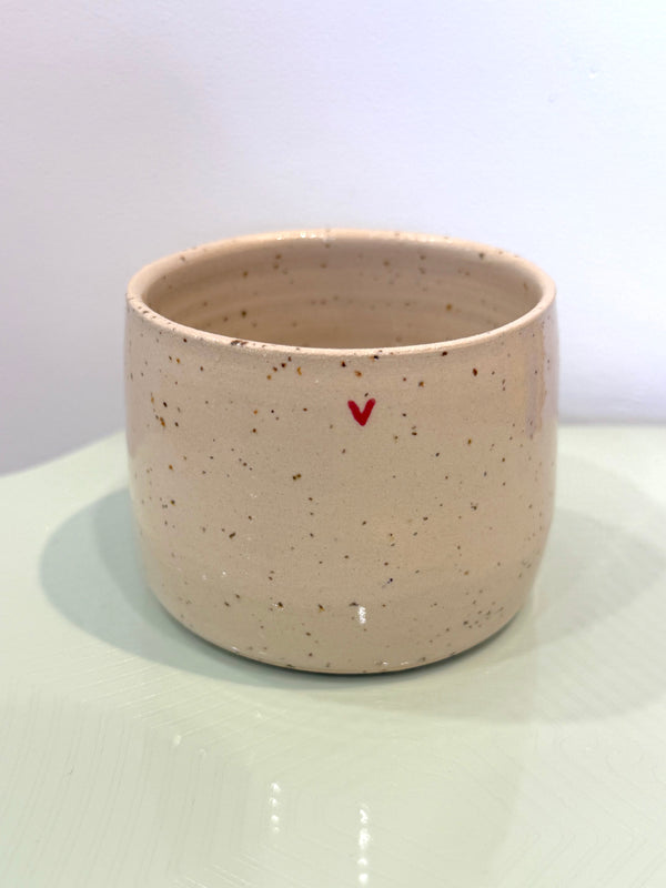 Speckled ceramic cup with a red heart on a white surface