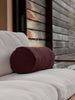 Burgundy linen bolster cushion resting on a neutral-toned outdoor sofa, styled in a modern, wooden deck setting.
