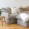 Light grey linen armchair styled in a cosy living space with neutral accents, wood furniture, and a fringed white throw.