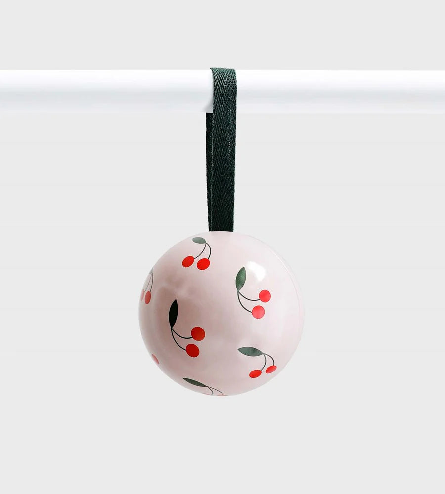 Soft pink ceramic ornament with a red cherry and green leaf pattern, hanging from a dark green ribbon against a light grey background