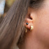 Close-up of a gold earring with a black gemstone and fine chain detail, styled with a thick gold ear cuff for a bold, layered look.