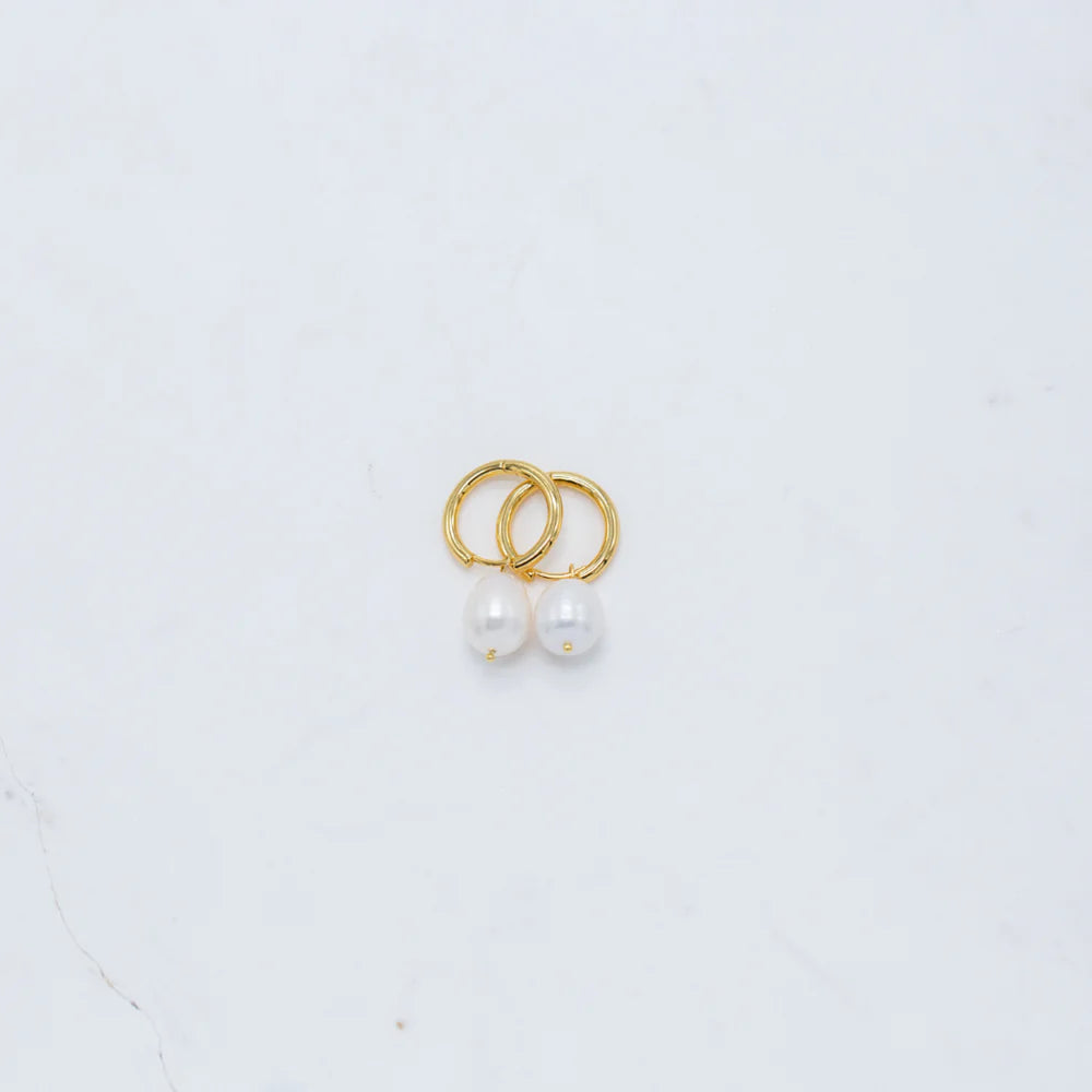 Gold hoop earrings with freshwater pearl drops, photographed on a white marble background.