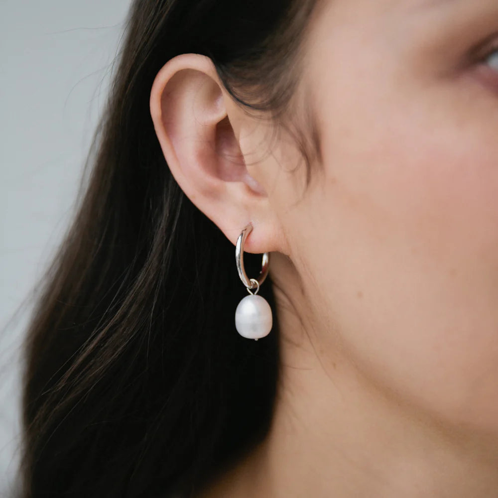 Sterling silver hoop earring with a single freshwater pearl drop, shown worn on ear.