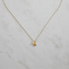 Delicate gold necklace featuring a small shell charm and pearl pendant, styled on a marble surface for a coastal-inspired, minimalist look.