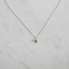 Minimalist silver necklace featuring a dainty shell charm and pearl pendant, styled flat on a light marble surface for an elegant, ocean-inspired look.