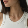 Gold shell and pearl necklace styled on a model with a white ribbed tank, showing a delicate and minimalist jewellery look.