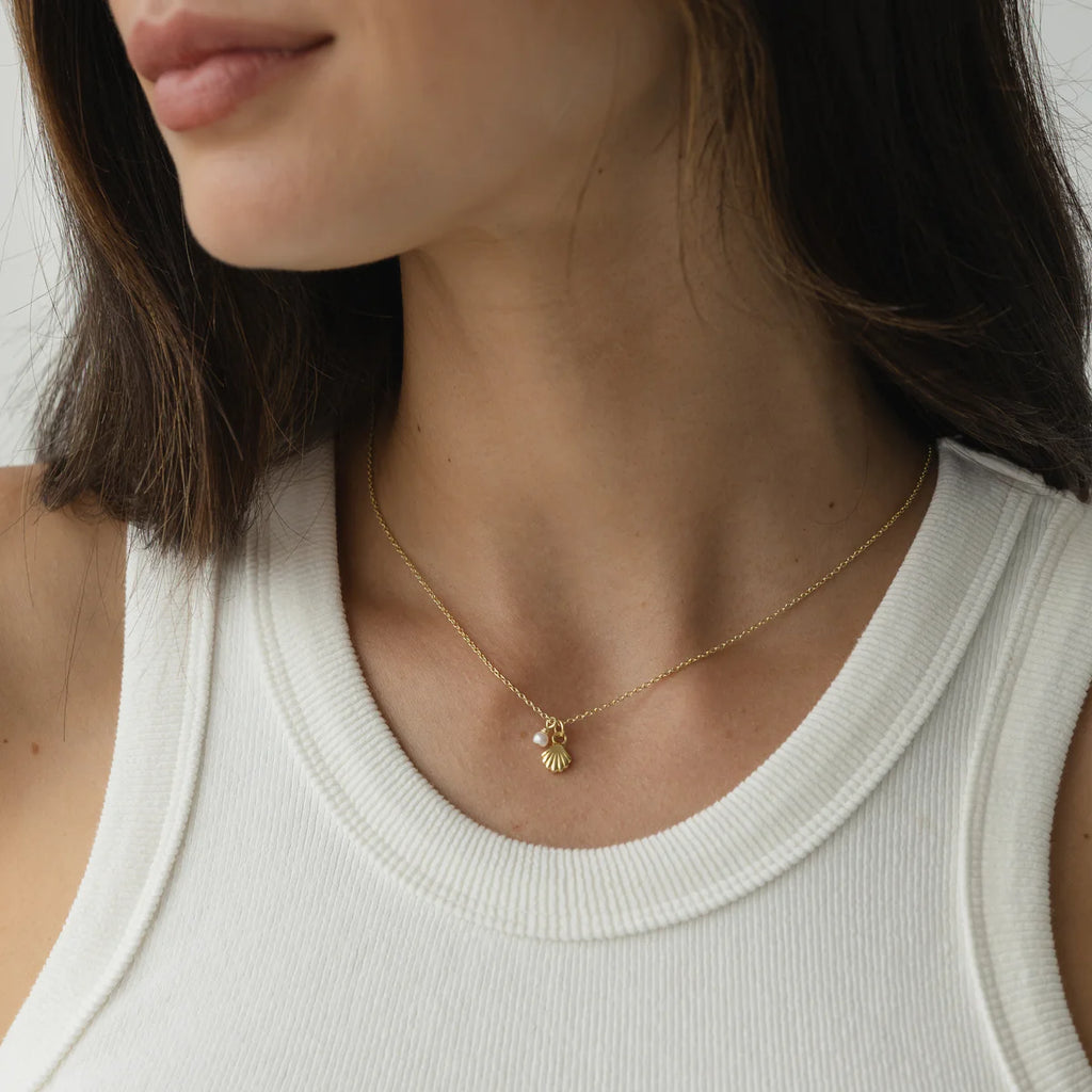 Gold shell and pearl necklace styled on a model with a white ribbed tank, showing a delicate and minimalist jewellery look.