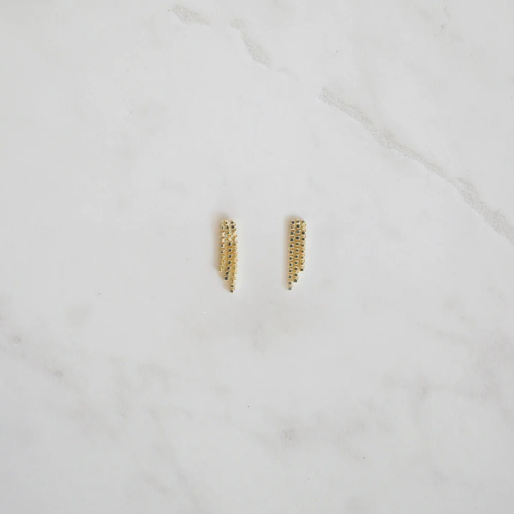 Gold crystal mesh fringe stud earrings laid flat on a white marble surface, showcasing their elegant drape and sparkle.