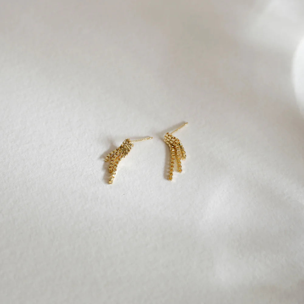 Gold chain fringe stud earrings displayed on a soft white fabric background, showcasing their delicate and elegant design.