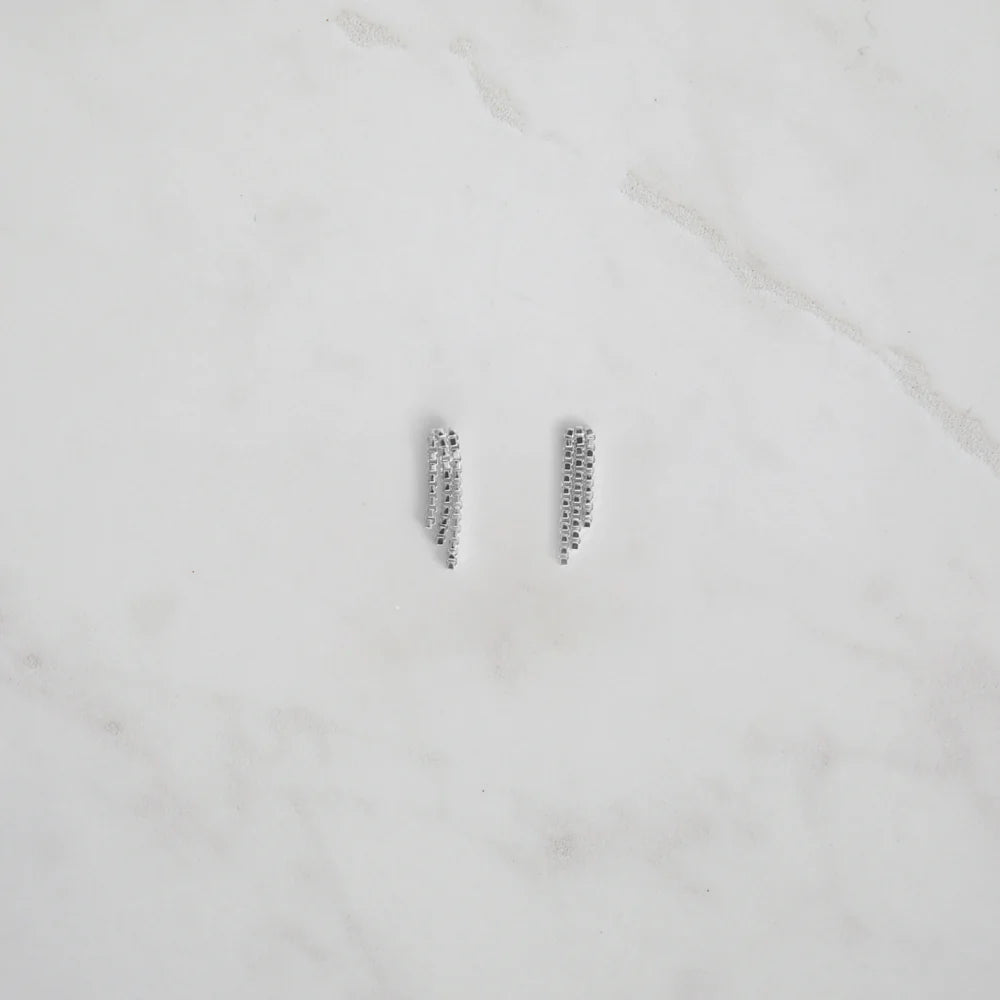 Silver crystal mesh fringe earrings laid flat on marble, showcasing their modern draped design and delicate sparkle.