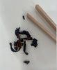 Loose leaf tea blend with dried fruit and petals next to wooden blending sticks – a DIY tea mixing flat lay.