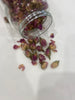 Glass jar spilling dried rose buds onto a white surface – a delicate tea blending ingredient or botanical garnish.