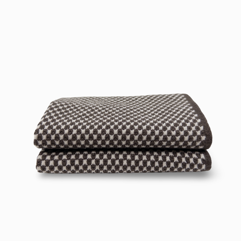 A folded cloth featuring a dark brown and light beige checkerboard pattern, set against a plain white background.