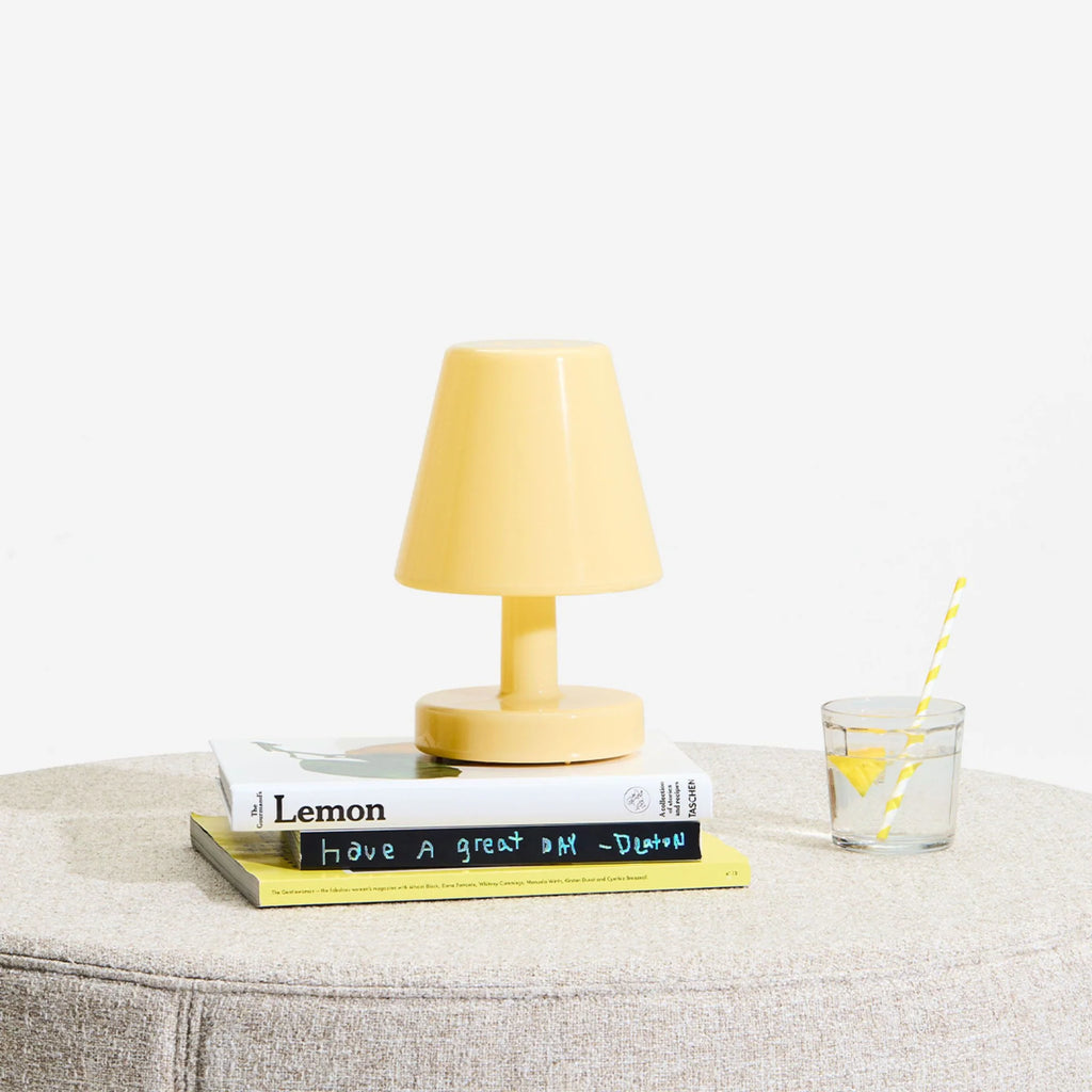 Yellow lamp on a stack of books with a glass of lemonade on a light gray surface.