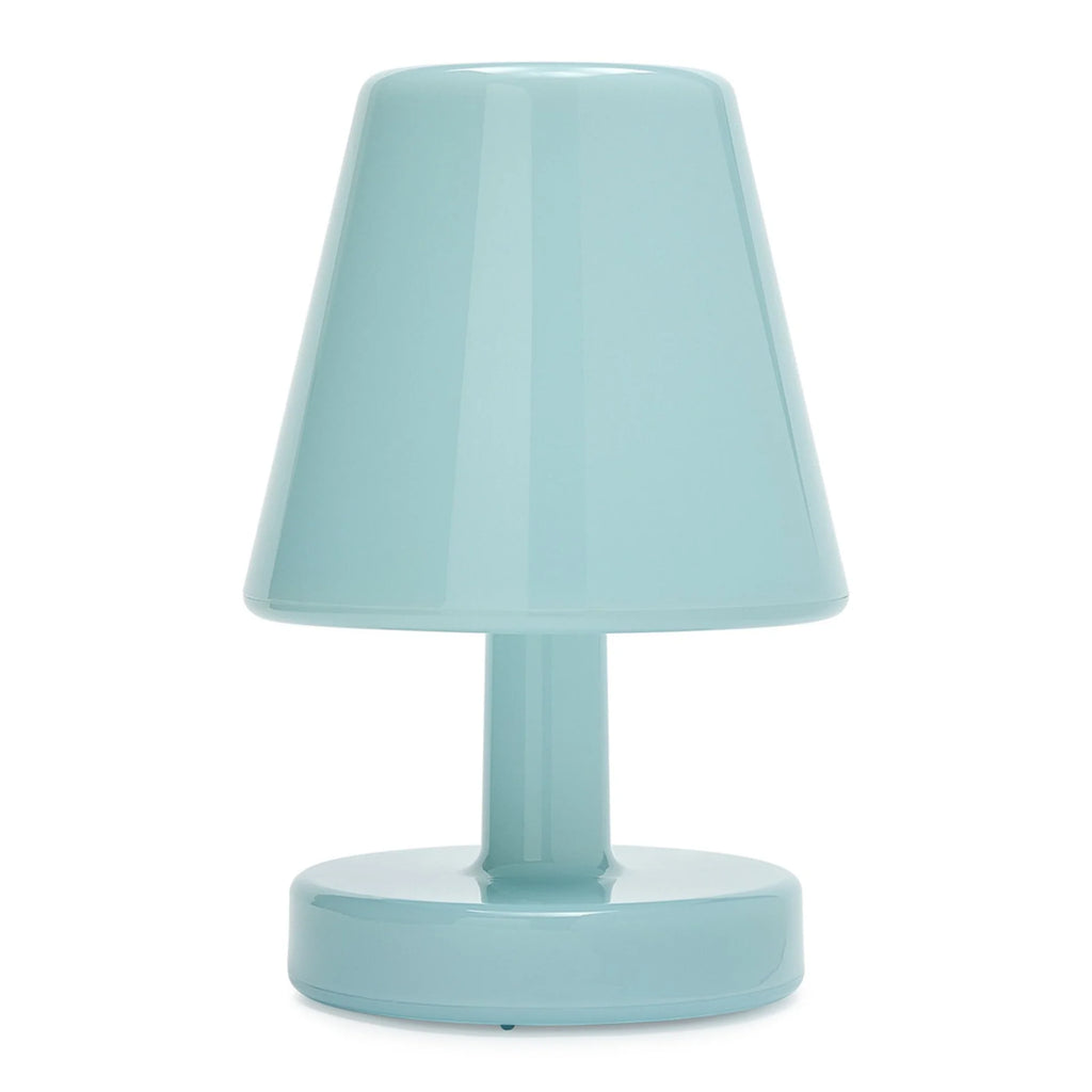 A small table lamp in a glossy light aqua or pastel blue color, featuring a tapered shade, a central stem, and a round base, shown against a plain white background.
