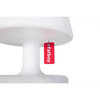 A red rectangular acrylic tag with the brand name 'fatboy' printed in white, hanging from a small metal ring under the edge of a white pedestal lamp.