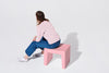 Person sitting on a pink stool against a white background