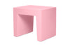 A minimalist pink side table with a geometric, block-like design and a hollow center, shown on a plain white background.