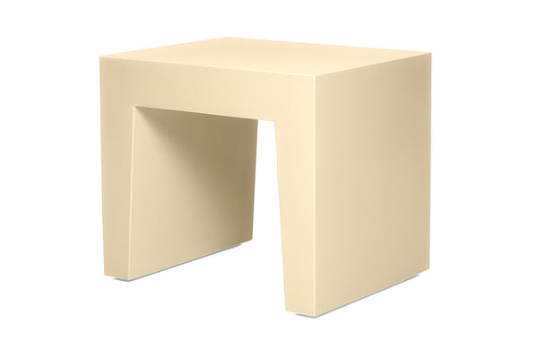 A modern, minimalist side table with a thick, blocky rectangular base in a warm cream or beige finish, isolated on a white background.