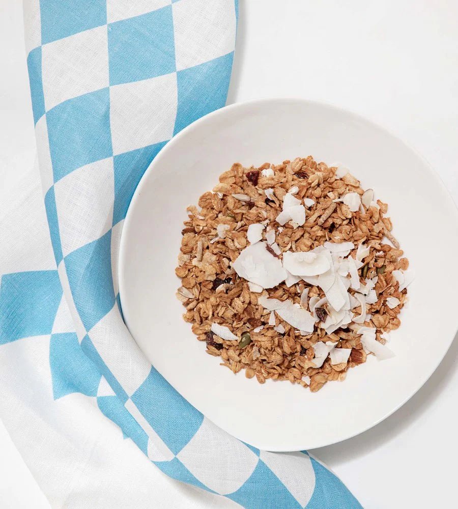 Close-up of a bowl of granola with coconut flakes on a blue and white diamond tea towel.