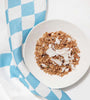 Close-up of a bowl of granola with coconut flakes on a blue and white diamond tea towel.