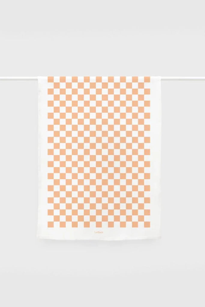 White tea towel featuring an orange checkerboard pattern, hanging neatly on a white rail with 'Lettermade' branding at the bottom.