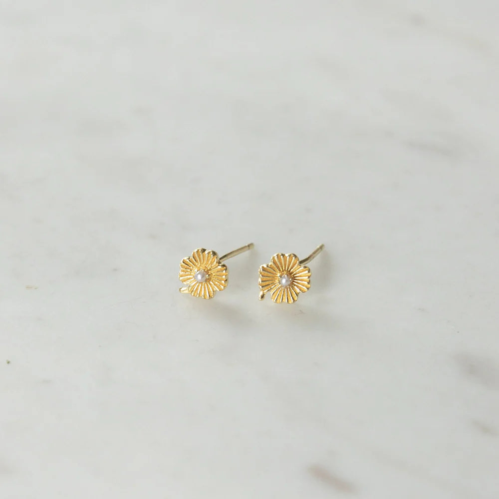Pair of gold lily earrings with pearl centers on a light grey background