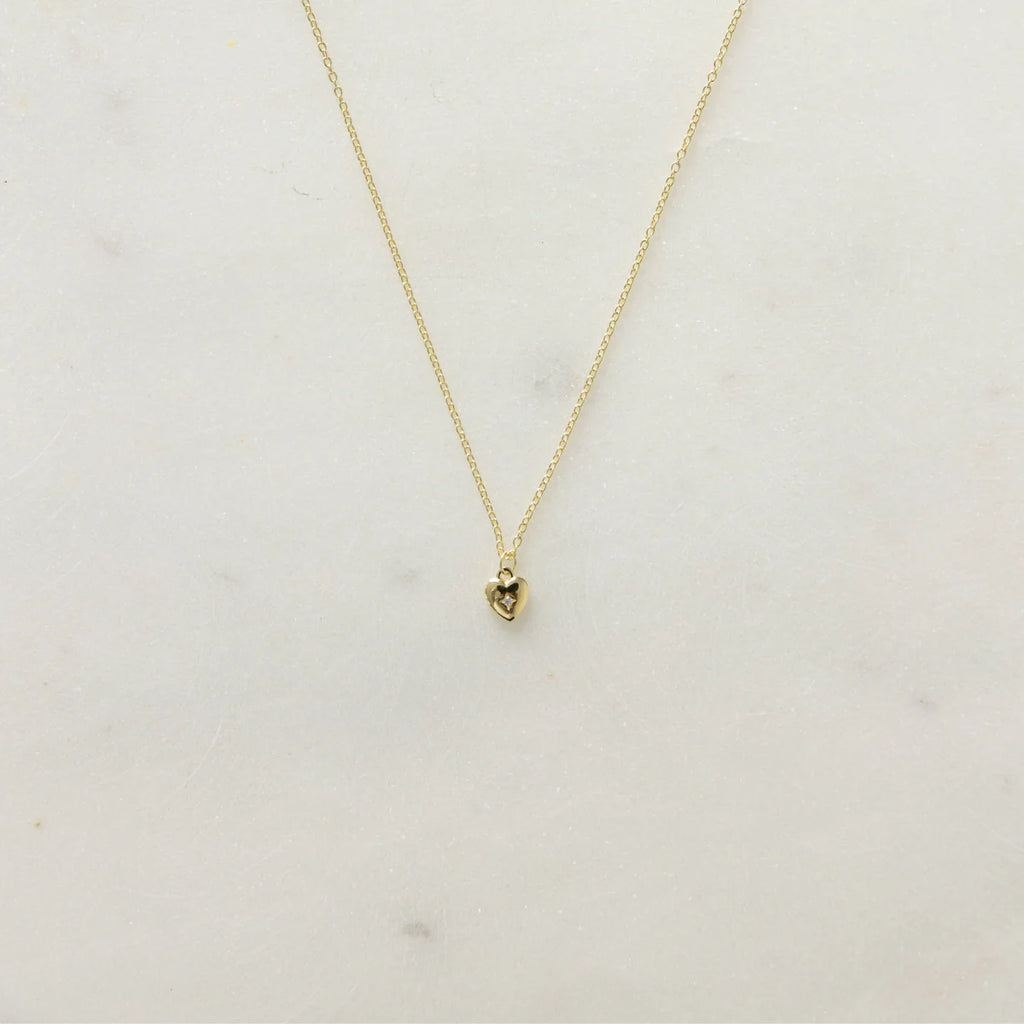Gold necklace with a heart pendant and small diamond on a light grey  background